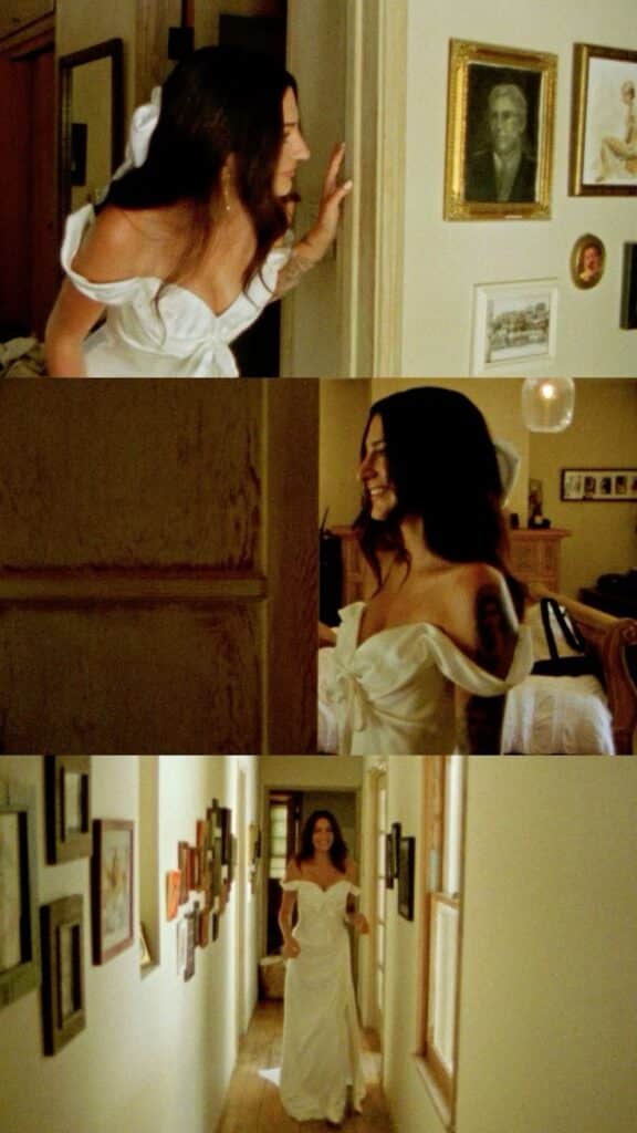 Woman in white off-shoulder dress exploring art in a hallway, smiling and joyful in a vintage setting.