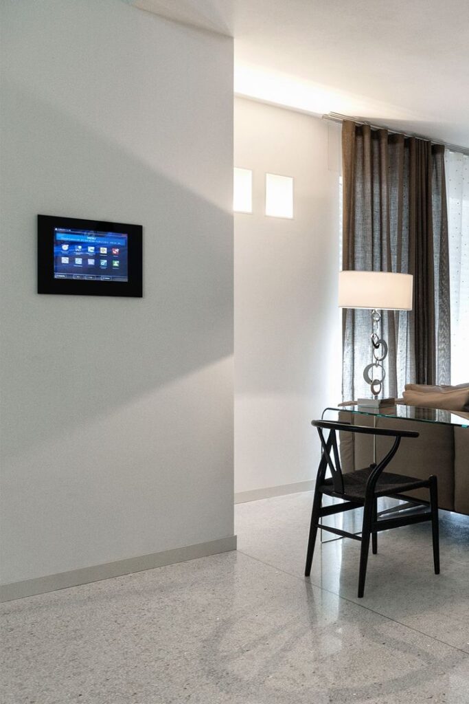 Modern living room with smart home control panel, glass desk, and elegant lighting.