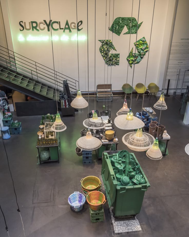 Recycling-themed showroom with hanging lights and green containers at Surcyclage, emphasizing eco-friendly design.