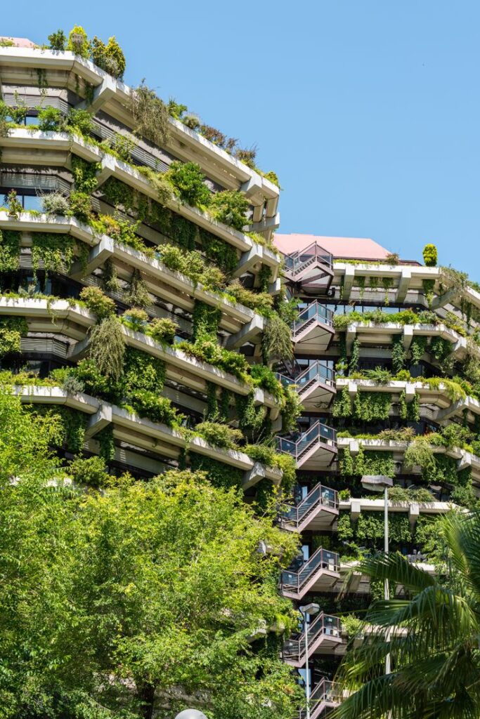 Eco-friendly building with lush green balconies and vertical gardens under a clear blue sky.