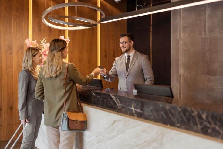 Hotel guests checking in at reception desk with friendly staff member in modern lobby setting.