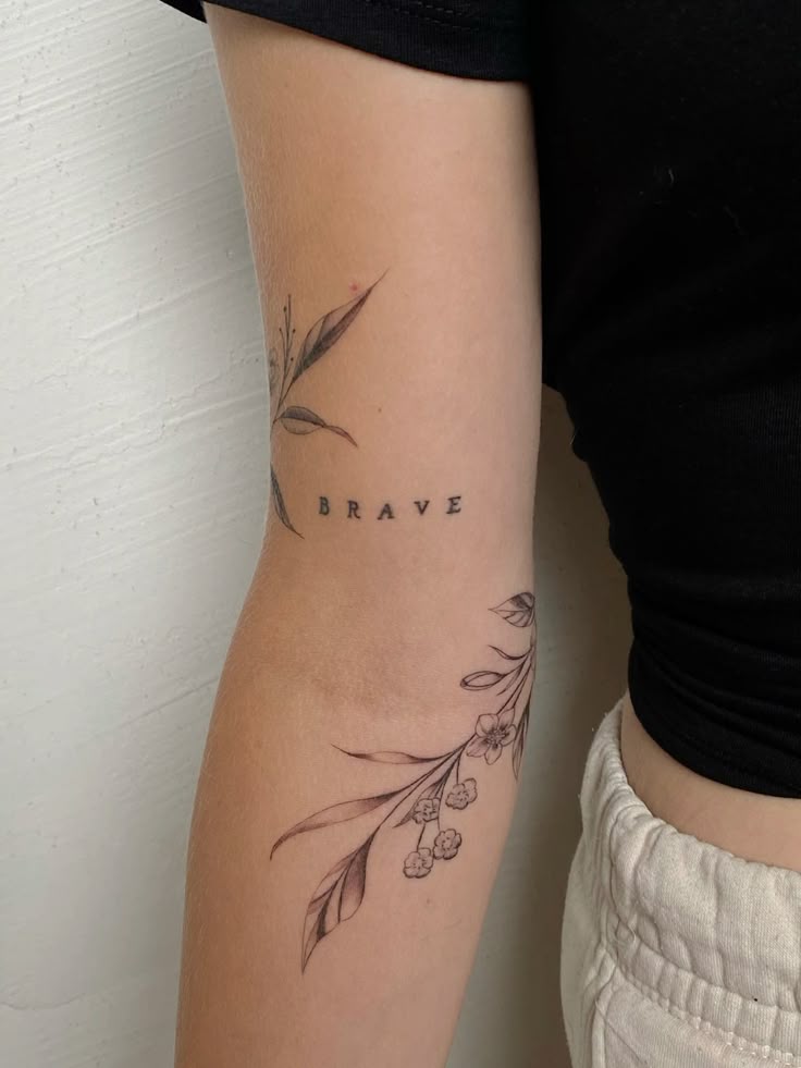 Tattoo 🤍 Arm with BRAVE and floral tattoo design, featuring detailed leaves and flowers. | Sky Rye Design Arm with BRAVE and floral tattoo design, featuring detailed leaves and flowers.