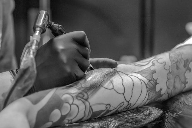 Tattoo artist creating intricate designs on an arm in a studio setting, close-up in black and white.