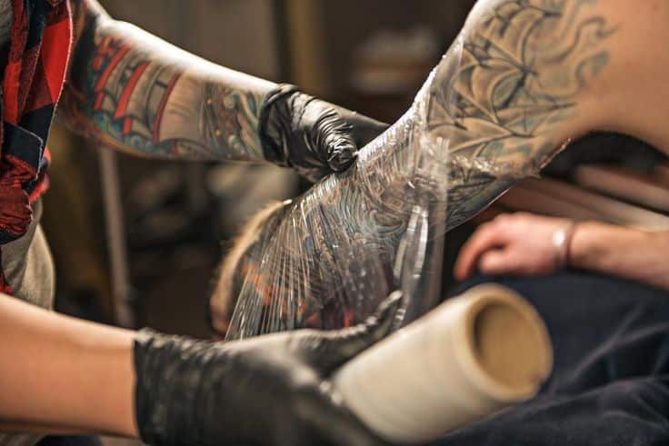 Tattoo artist wraps tattooed arm in protective plastic, enhancing color preservation and healing.