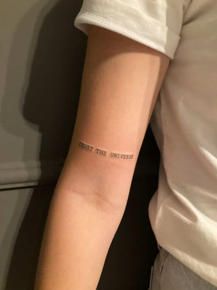 Minimalist Trust the Universe tattoo on arm in black ink, emphasizing positivity and belief.