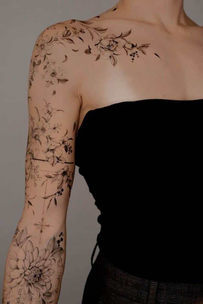 Floral tattoo sleeve on woman's arm, with detailed flowers and leaves, wearing a black top.