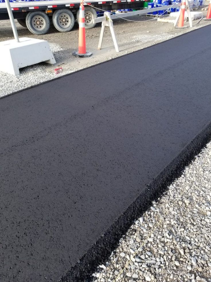 Freshly paved asphalt road section under construction, marked by orange cones and gravel in the foreground.