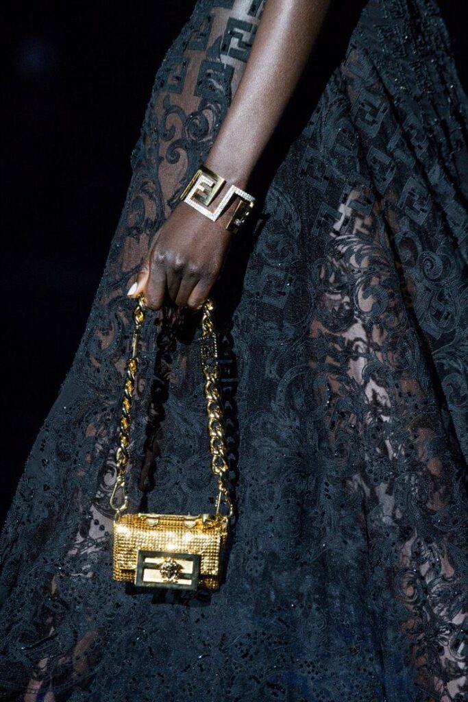 The Swap - Fendace _ Official Website Elegant lace dress with gold chain handbag and geometric bracelet on a fashion runway. | Sky Rye Design Elegant lace dress with gold chain handbag and geometric bracelet on a fashion runway.