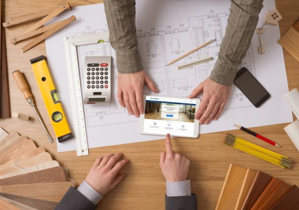Architects reviewing building plans on a tablet surrounded by tools and samples on a wooden desk.
