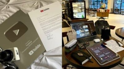YouTube Silver Play Button with camera, letter, laptop, and tablet setup in a cozy cafe workspace.