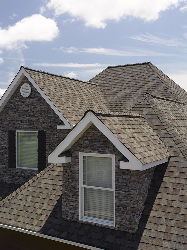 Stone house with brown shingle roof and dormer windows under a blue sky.