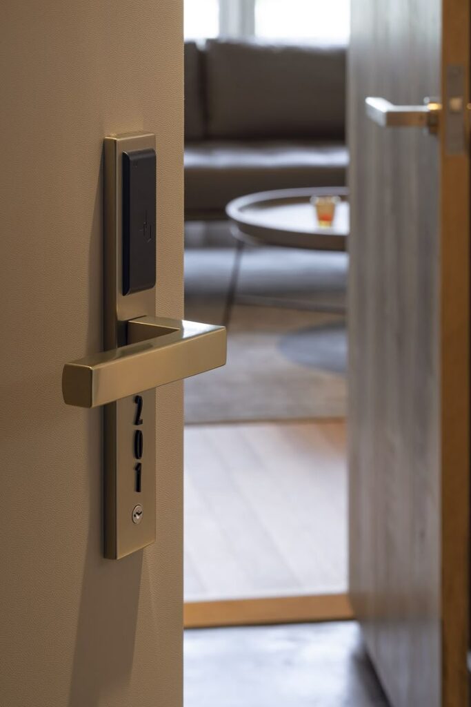 Modern hotel room door with digital lock and handle, partially open to a cozy interior with a table and couch.