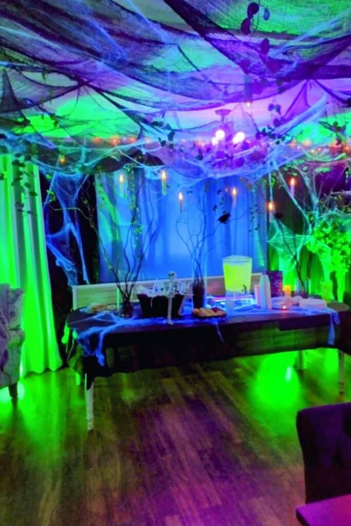 Spooky Halloween party decor with glowing green and purple lights, cobwebs, and a festive buffet table.