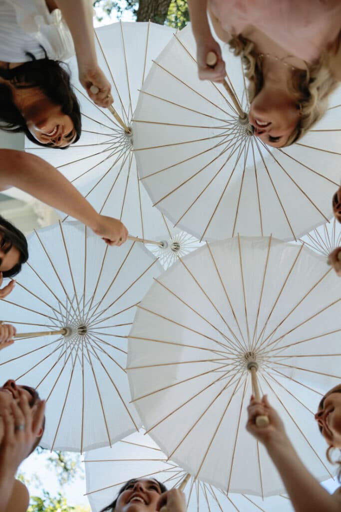 Women smiling under white parasols, viewed from below, against a sunny sky.