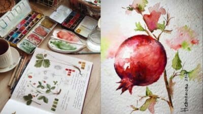 Artist's workspace with watercolor set and pomegranate painting, featuring a botanical sketchbook and a cup of tea.