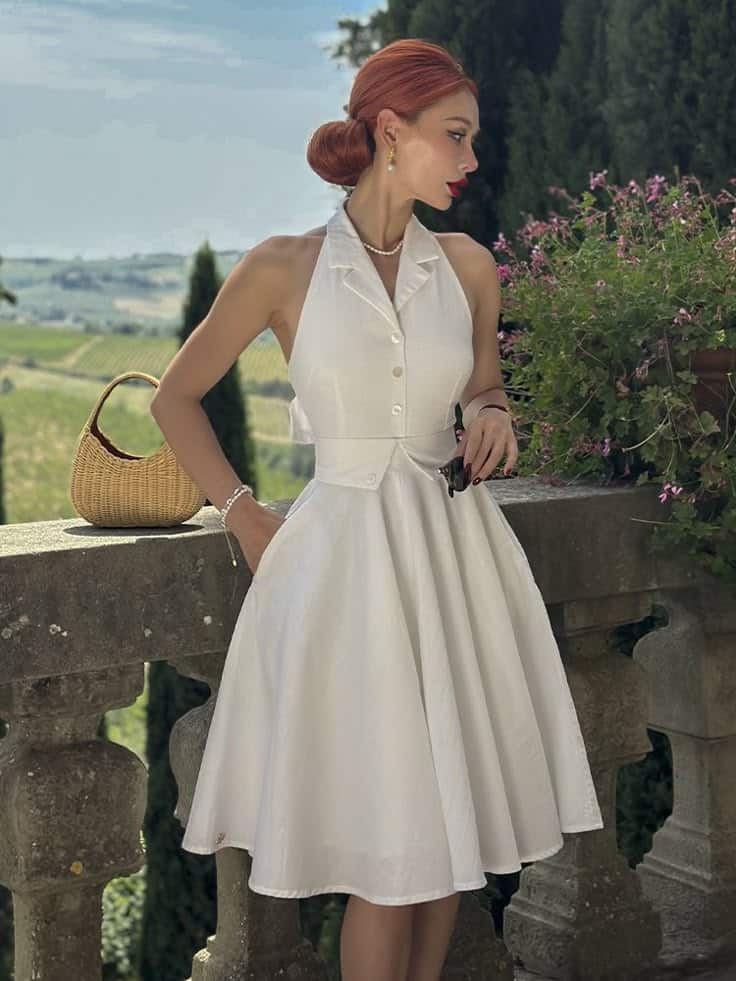Woman in elegant white dress and red hair, standing on balcony with scenic countryside view.