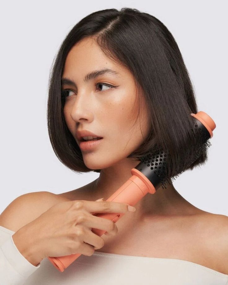 Woman styling short hair with a round brush for a sleek look. Hair care and grooming.