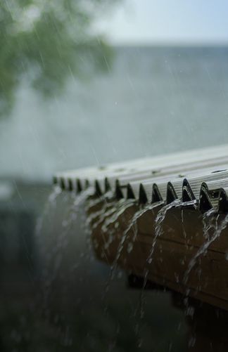 Rainwater cascading off a roof edge, illustrating heavy rainfall and outdoor weather dynamics.