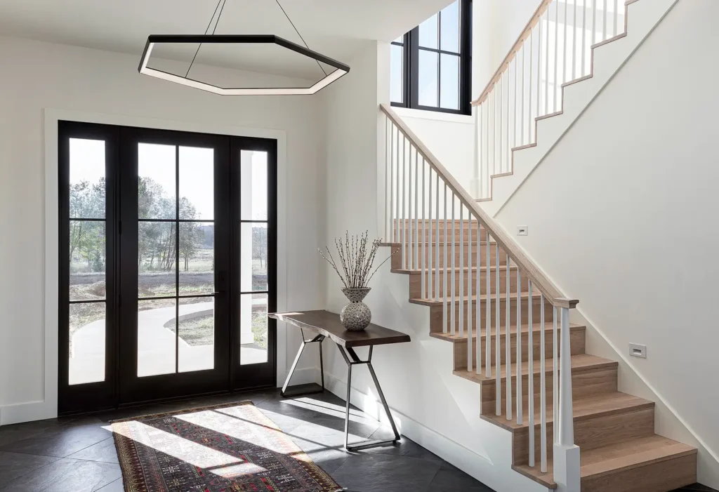 Washougal-Cover Modern foyer with wooden stairs, dark double doors, hexagonal light fixture, and decorative table with vase. | Sky Rye Design Modern foyer with wooden stairs, dark double doors, hexagonal light fixture, and decorative table with vase.