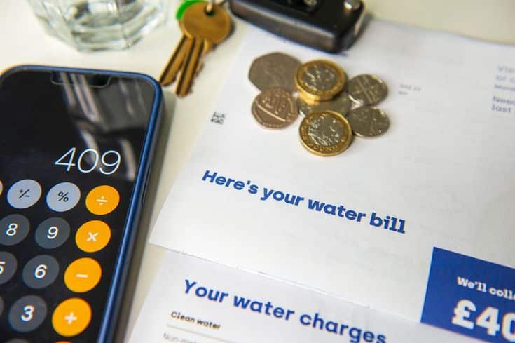 Water bill warning as major report to shake-up_ Phone displaying calculator app, water bill, coins, and keys on a table, symbolizing budgeting and expenses. | Sky Rye Design Phone displaying calculator app, water bill, coins, and keys on a table, symbolizing budgeting and expenses.