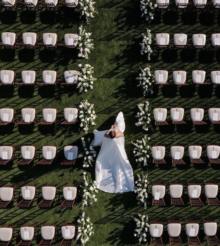 Bride walking among arranged chairs in an outdoor wedding venue, surrounded by white flowers and greenery.