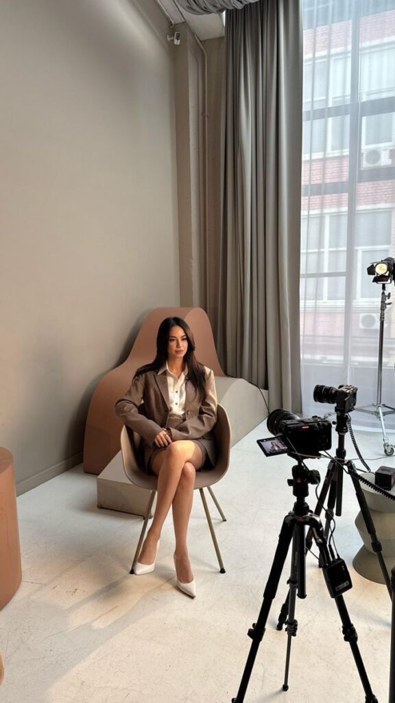 Businesswoman in beige suit sitting for a professional photo shoot in a modern studio setting.