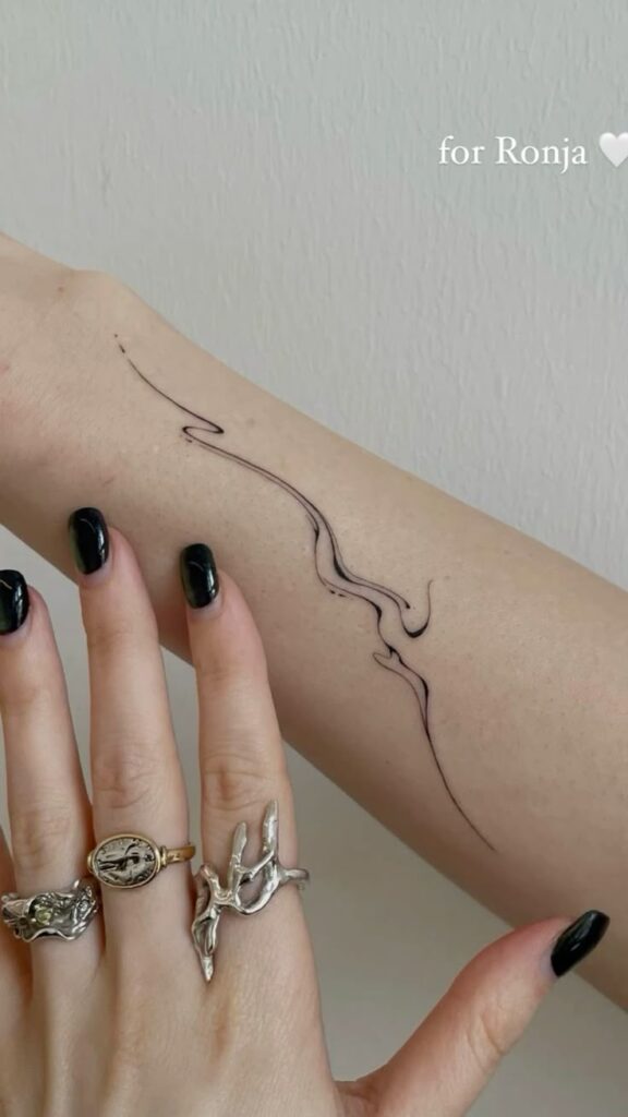 Abstract line tattoo on arm with rings and black nail polish. Simple, elegant tattoo design.