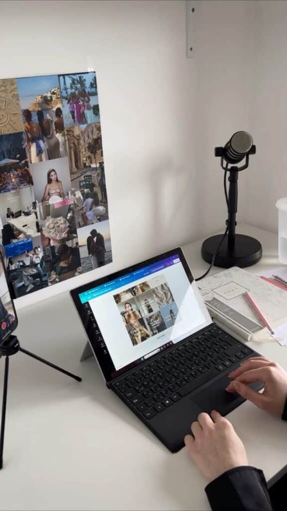 Person using a laptop on a desk with mood board, microphone, and planner in a workspace setting.
