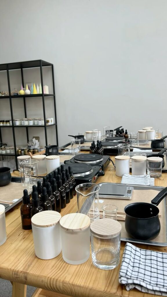 Candle-making workshop setup with jars, beakers, droppers, and hot plates on wooden tables in a studio setting.