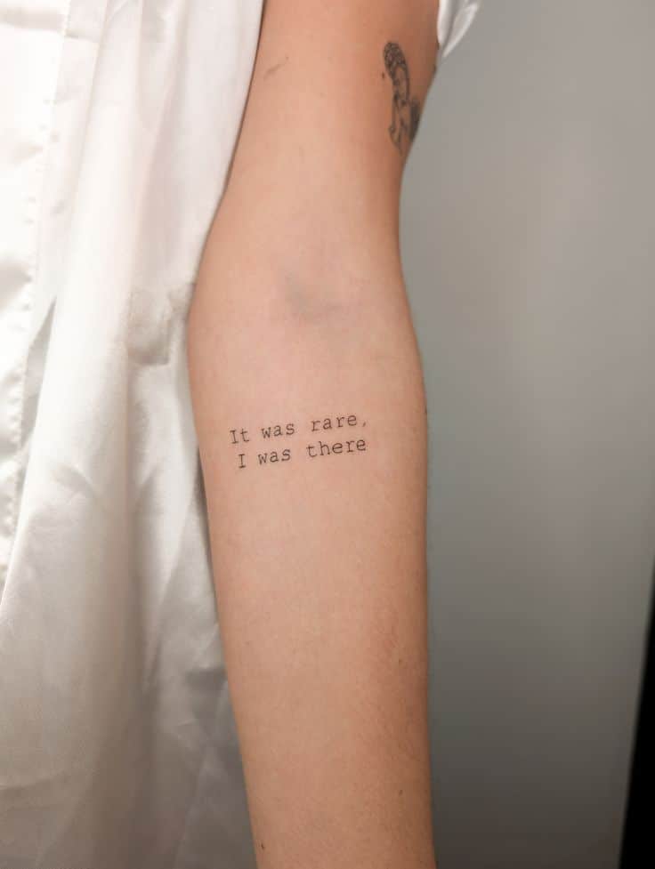 Arm with tattoo reading It was rare, I was there, beside white fabric. Minimalistic black ink design.