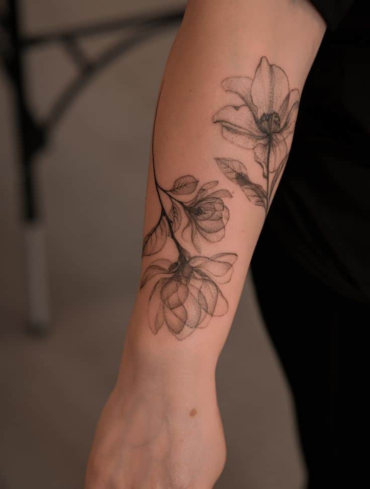 Delicate floral tattoo on forearm, featuring detailed magnolia blossoms in black ink.