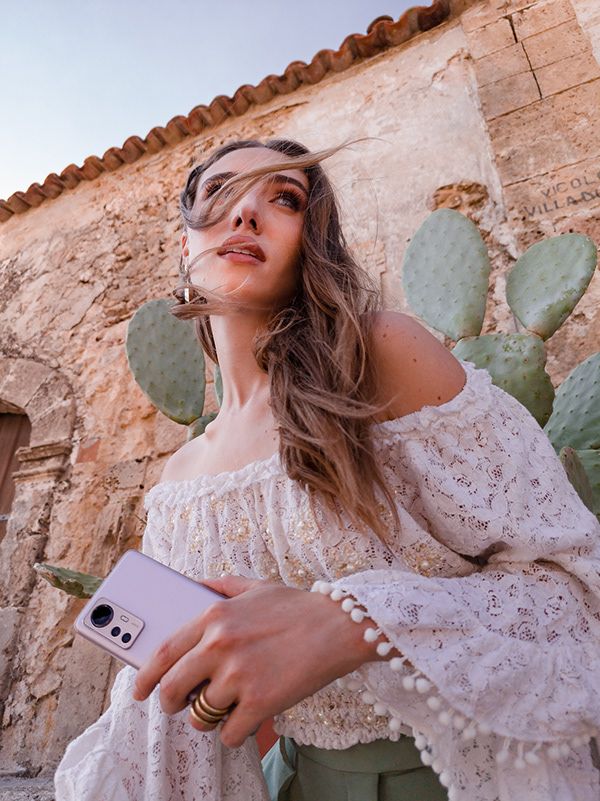 Xiaomi 12 Pro Campaign 2022 - AD Commercial - Nelb Rodrigues Young woman in a white lace top holding a smartphone, standing in front of a rustic stone wall and cactus. | Sky Rye Design Young woman in a white lace top holding a smartphone, standing in front of a rustic stone wall and cactus.