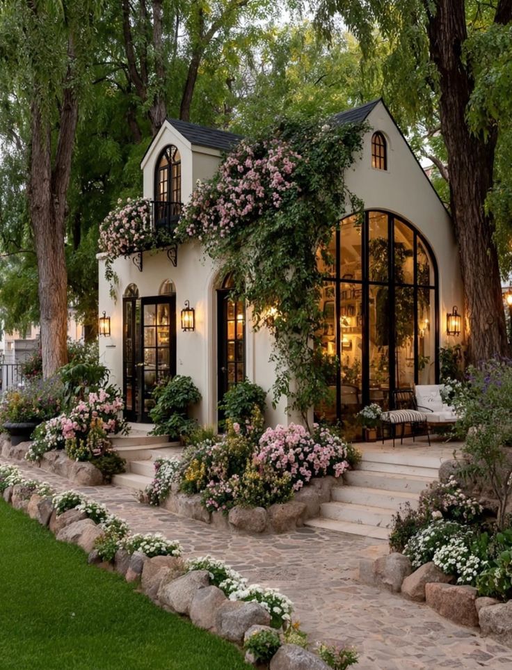 Charming cottage with lush garden and blooming flowers, set amidst tall trees and natural stone path.