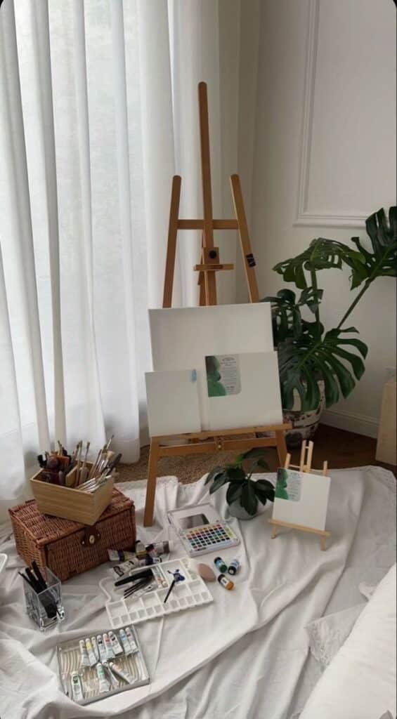 Art supplies and easel ready for painting in a cozy studio space with natural light and plants.