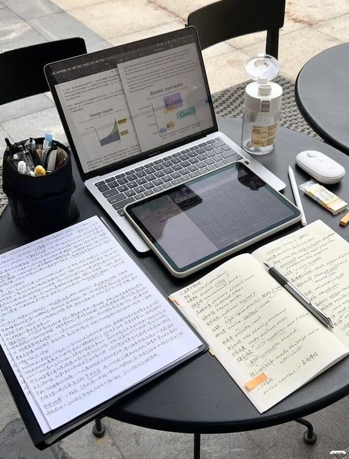 Laptop and tablet on a table with notes and a water bottle, ideal for outdoor study or work sessions.
