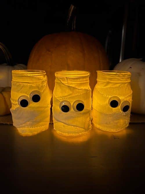 a4f468e1adcee4550e6e43a21763c360 Three glowing mummy-themed jars with googly eyes, perfect for Halloween decoration against a pumpkin backdrop. | Sky Rye Design Three glowing mummy-themed jars with googly eyes, perfect for Halloween decoration against a pumpkin backdrop.