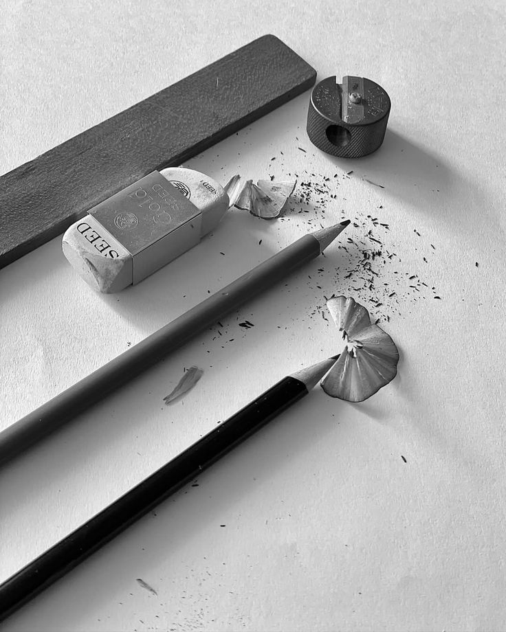 Black and white image of pencils, eraser, sharpener, and shavings on a white surface.