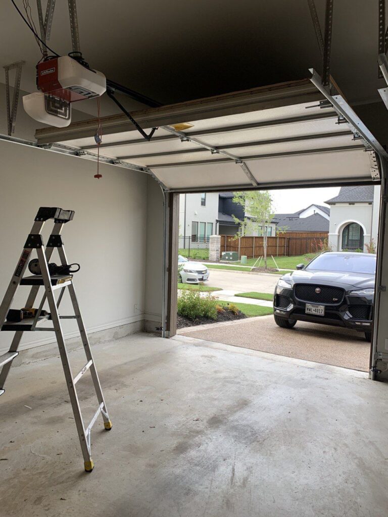 Open garage view with a parked car outside and a ladder inside, showcasing a residential suburban setting.