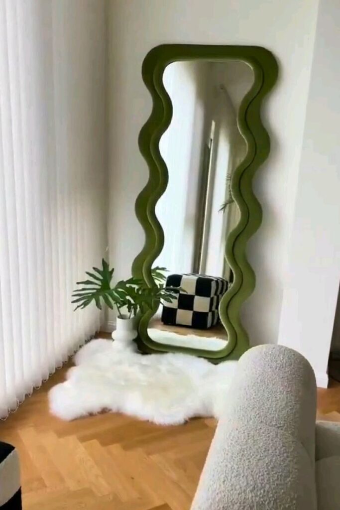 Wavy green mirror in modern room with checkerboard ottoman and white fluffy rug on wooden floor.