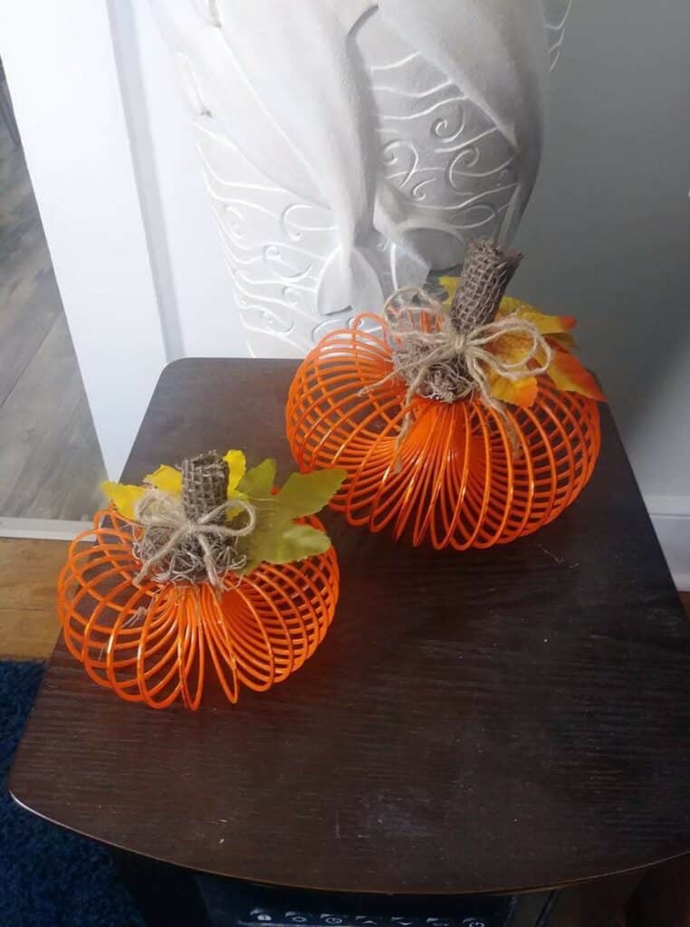Decorative orange wire pumpkins with burlap stems and leaves on a dark wooden table.