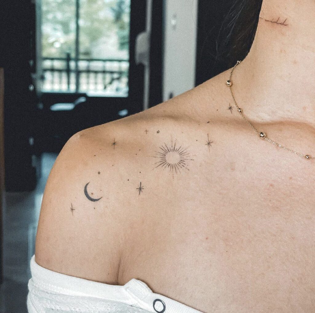 Minimalist celestial tattoos on shoulder, featuring sun, moon, and stars, against a soft background.