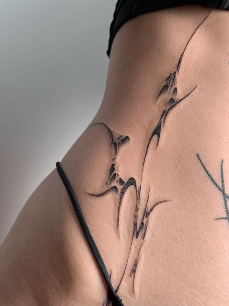 Abstract line tattoo on a person's hip, showcasing intricate black ink design and smooth skin texture.