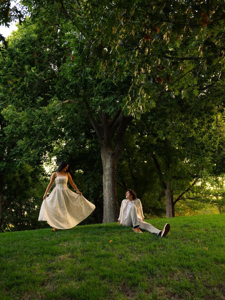 A couple enjoys a sunny day in a lush green park, the woman twirls in a flowing dress while the man relaxes on the grass.