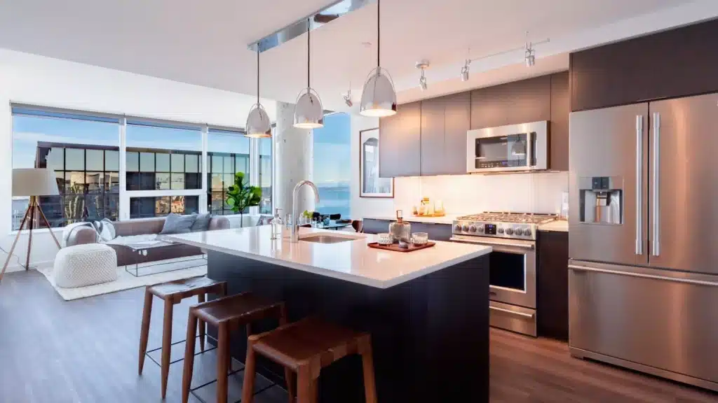 arrive-unit-3611-00004-1920x1080jpg Modern kitchen with island, pendant lights, stainless steel appliances, and a cozy living area with large windows. | Sky Rye Design Modern kitchen with island, pendant lights, stainless steel appliances, and a cozy living area with large windows.