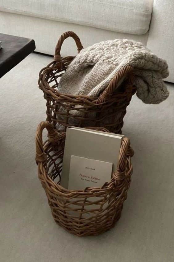 Woven baskets with a cozy knit blanket and a book on a carpeted floor in a minimalist living room setting.
