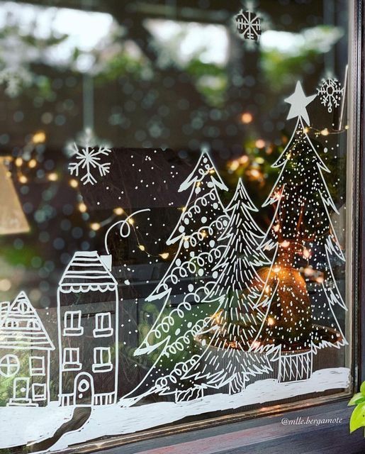 Festive Christmas window painting with snowy village, trees, and twinkling lights. Holiday decoration scene.