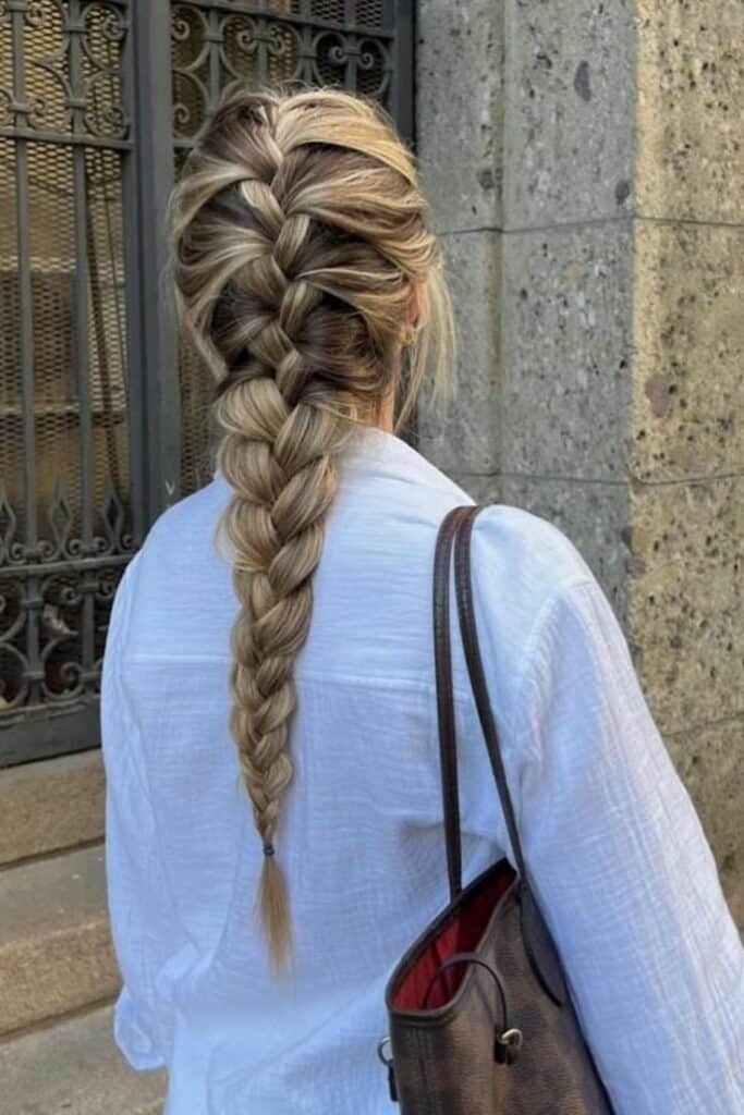 Woman with long braided hair in white blouse, carrying a brown handbag, outdoors.