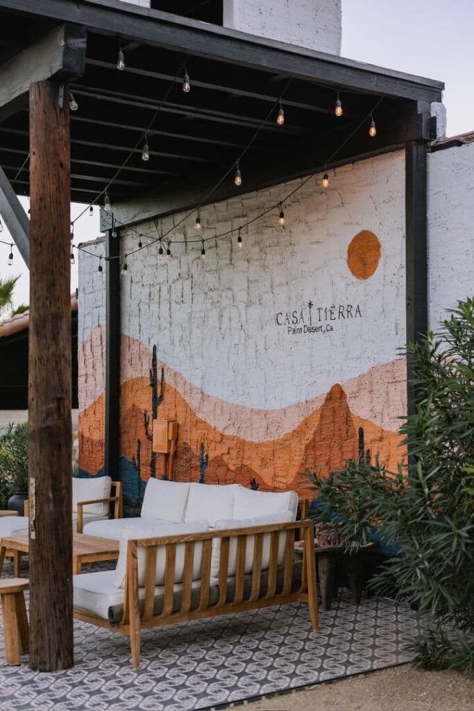 Outdoor lounge area with desert mural and string lights at Casa Tierra in Palm Desert, CA.