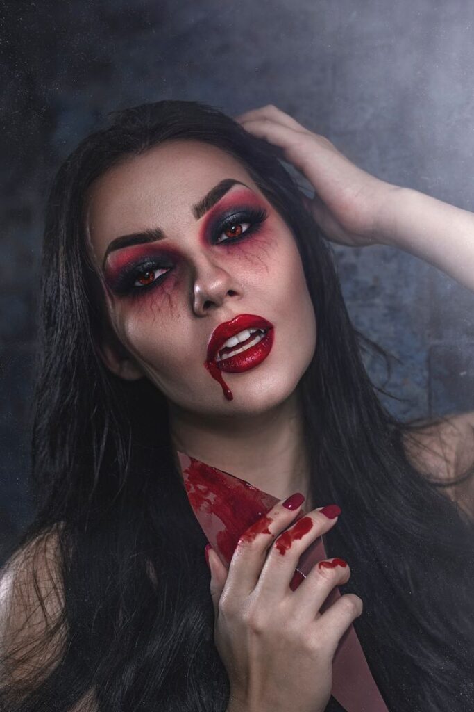 Vampire woman with dramatic makeup holding a blood-stained knife, dark and eerie atmosphere.
