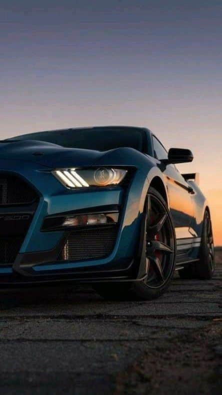 Close-up of a sleek blue sports car at sunset on a road, featuring modern headlights and a powerful, aerodynamic design.